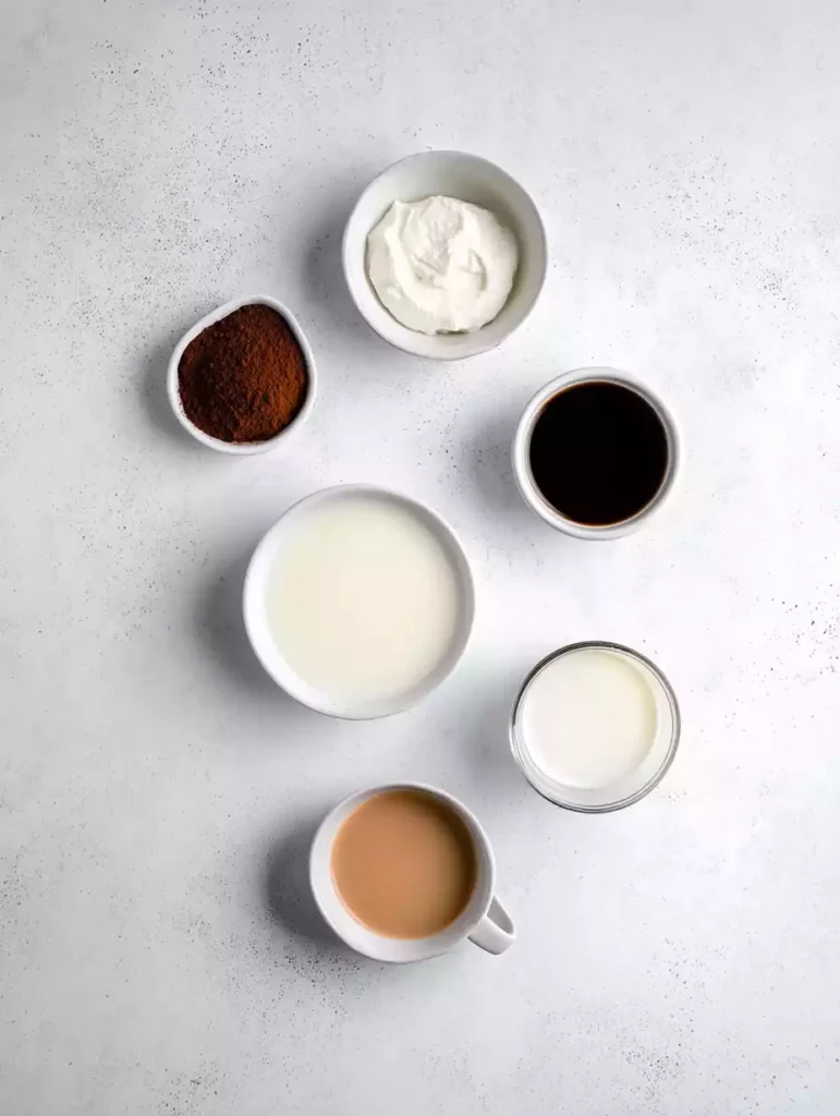 Flat lay of tiramisu latte ingredients including mascarpone, cocoa powder, espresso, milk, and cream