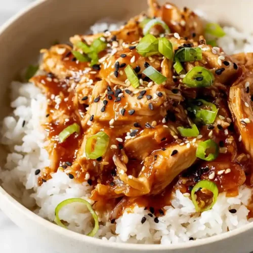 Bowl of honey garlic chicken thighs over steamed white rice topped with green onions and sesame seeds