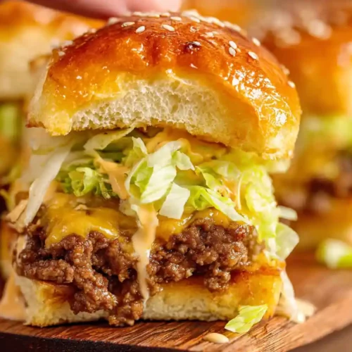 hand holding juicy Big Mac slider with sesame bun, lettuce, pickles, and melted cheese