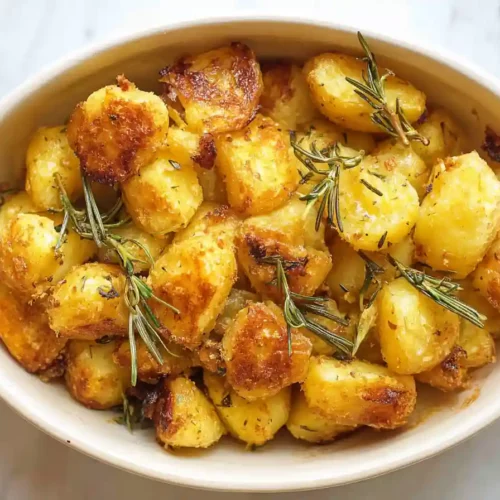 crispy roasted potatoes with rosemary sprigs in a red-handled baking dish on a white marble surface