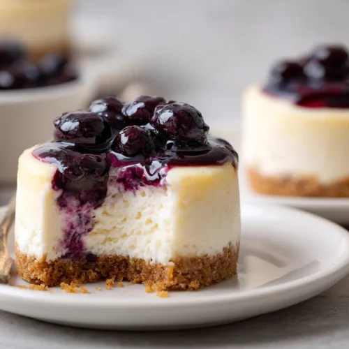 Mini lemon blueberry cheesecakes topped with fresh blueberries and a lemon zest