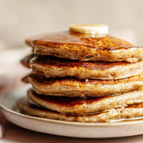 A stack of healthy banana oatmeal pancakes topped with fresh bananas and syrup